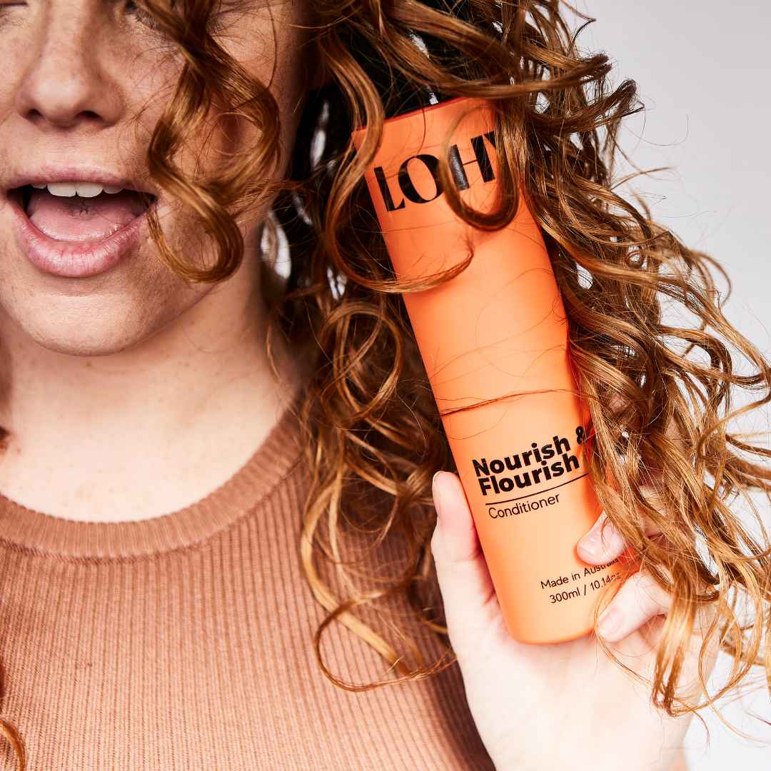 Bottle of conditioner held amongst beautiful orange curls